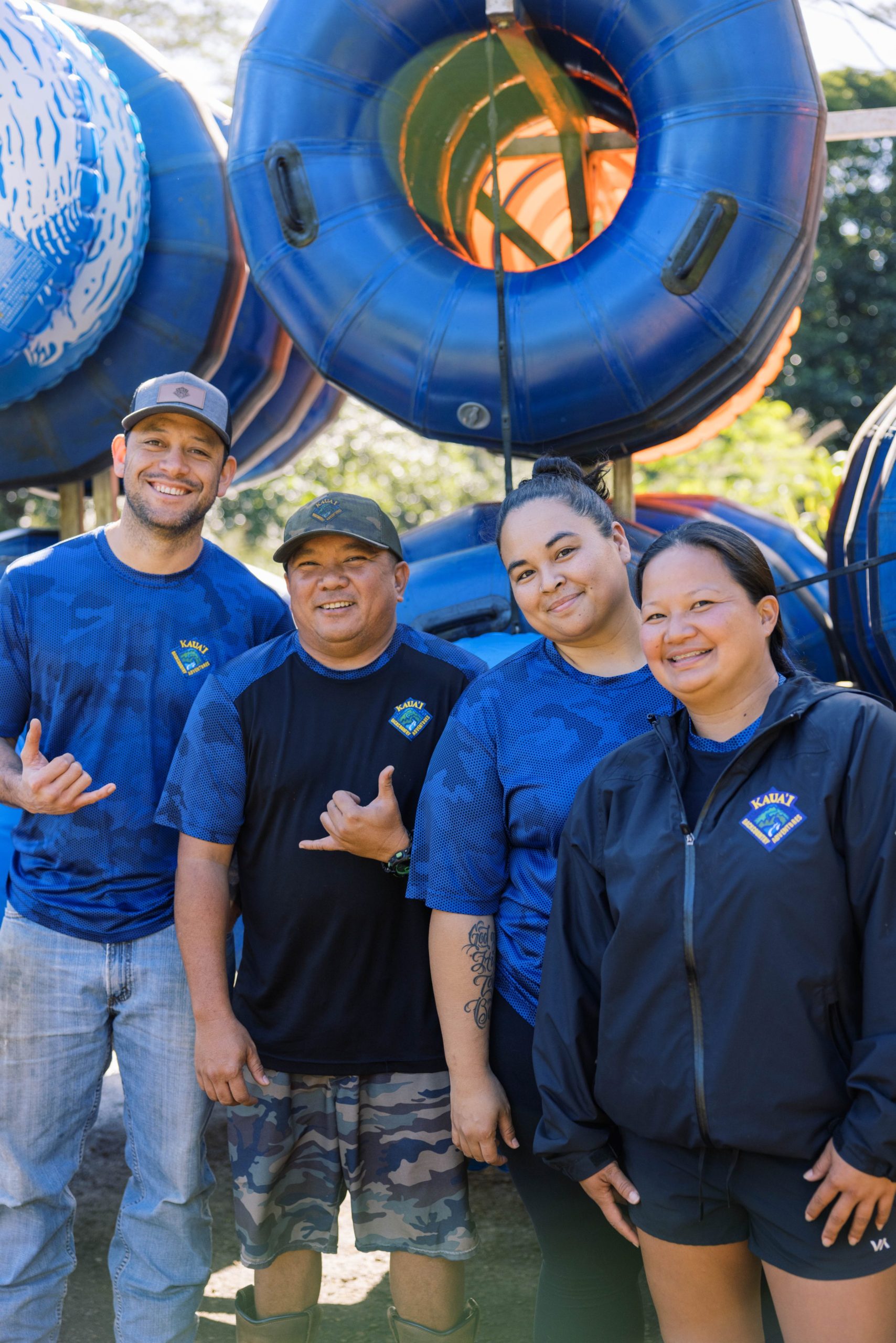 Four people smiling in front of stacked blue tubes outdoors.