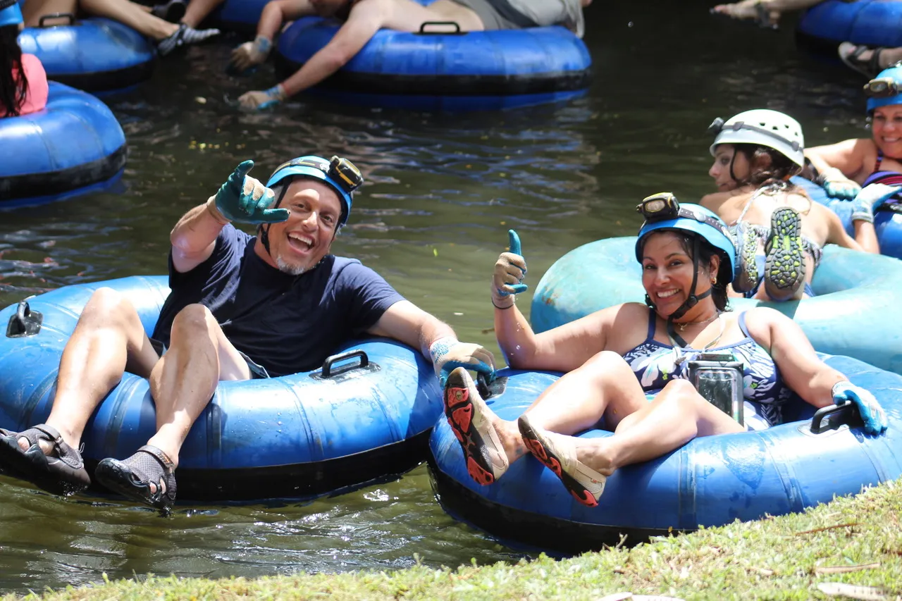 People tubing on a river, smiling and gesturing with thumbs up.