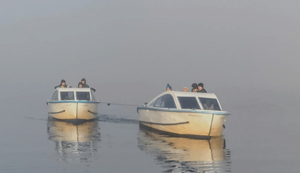 Two white boats on calm water, misty background.