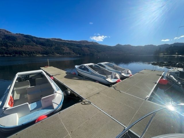Upside-down image of boats docked at a marina with mountains and clear sky in the background.