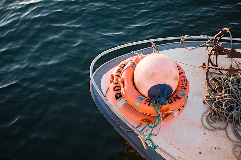 Boat bow with life ring and buoy on calm water.