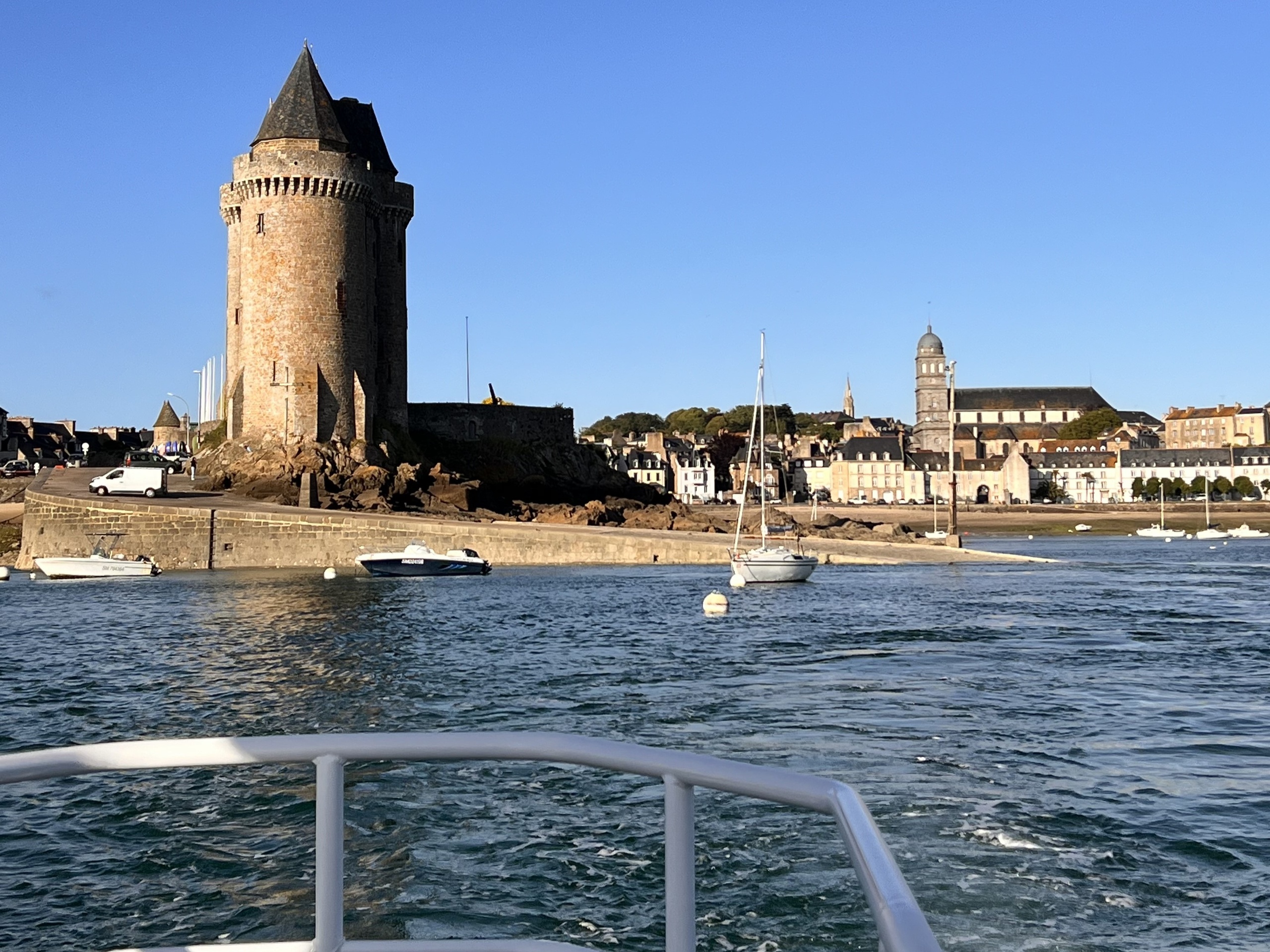 Harbor view with a tall stone tower, boats, and coastal town in the background.