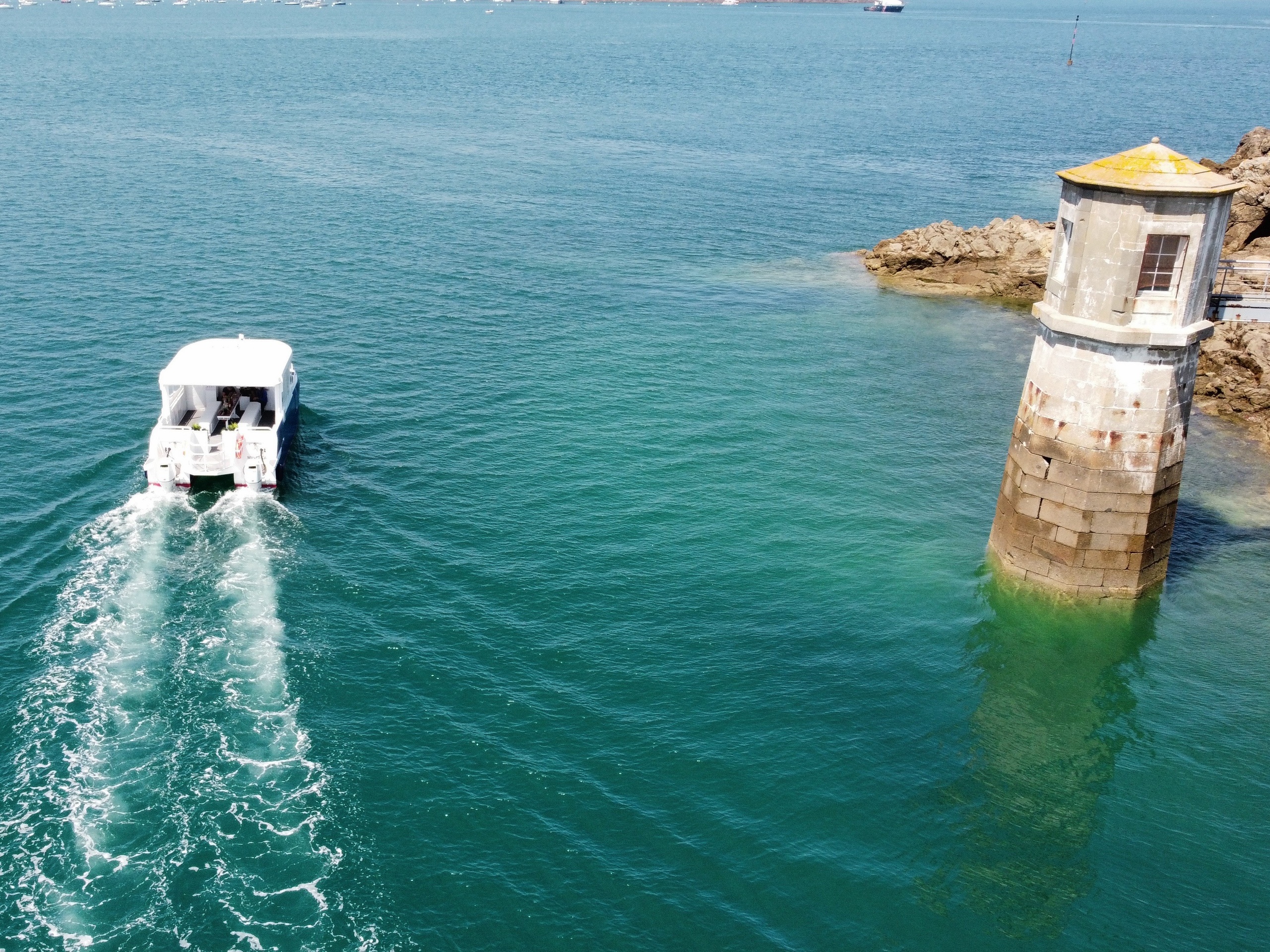 Boat passing near a small lighthouse on rocky coast in a calm sea.