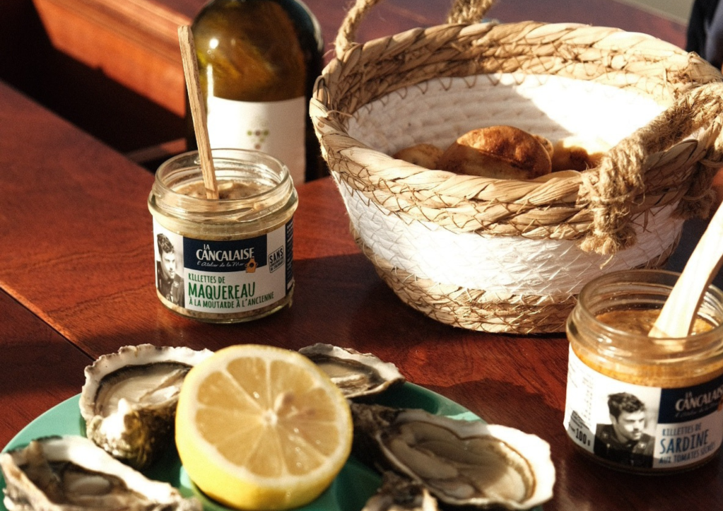 Oysters, lemon, jars, bread basket, and bottle on a table.