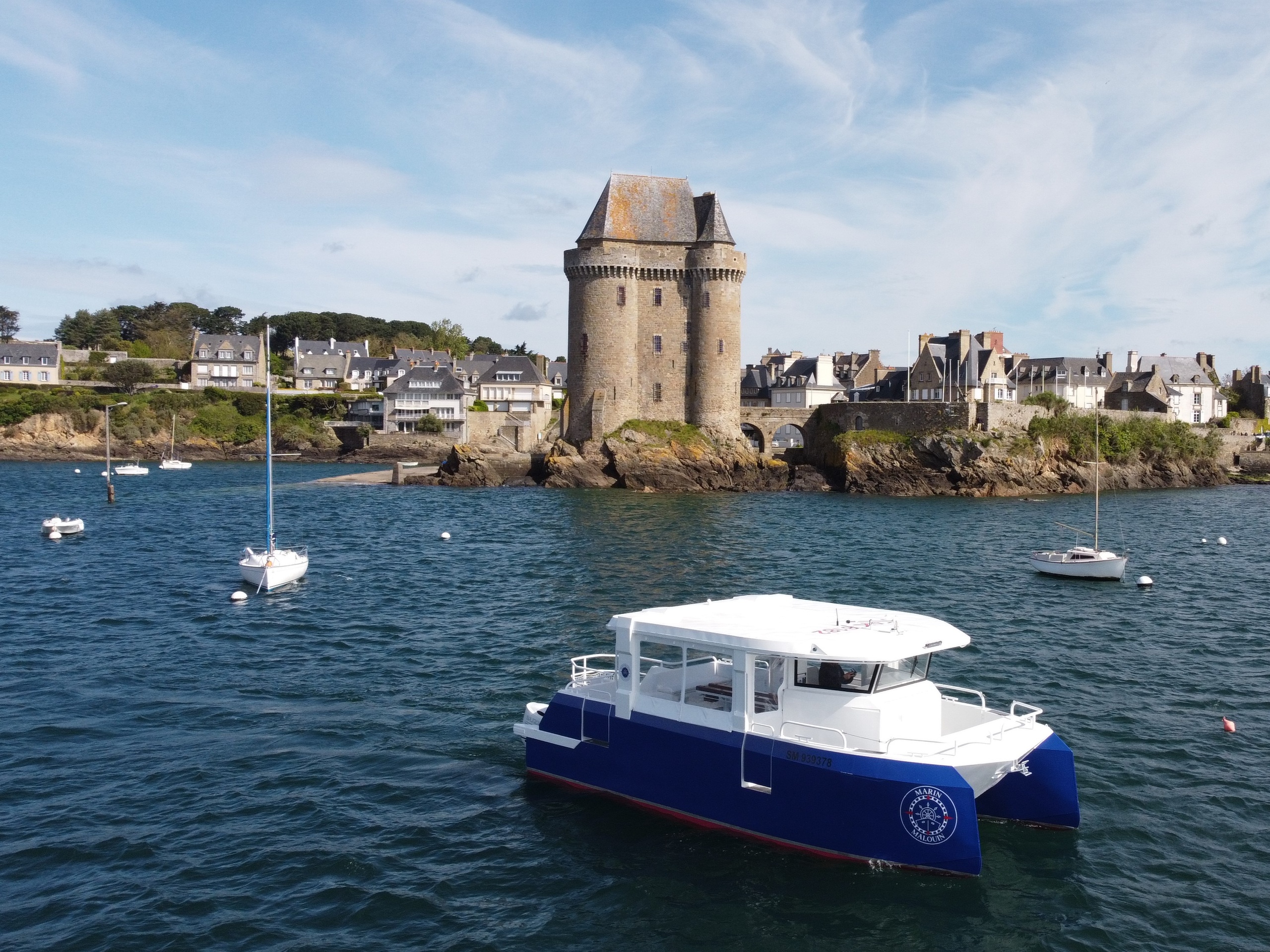 Catamaran in a harbor with a stone tower and houses in the background.