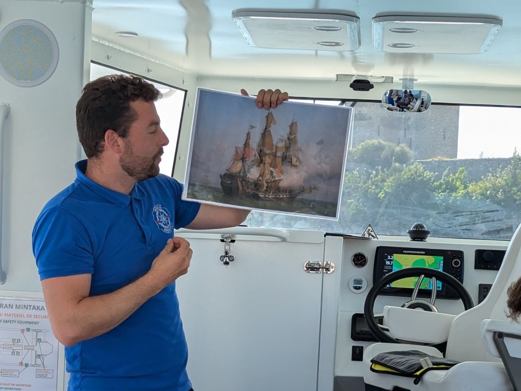 Man in blue shirt holding a ship painting inside a boat cabin.