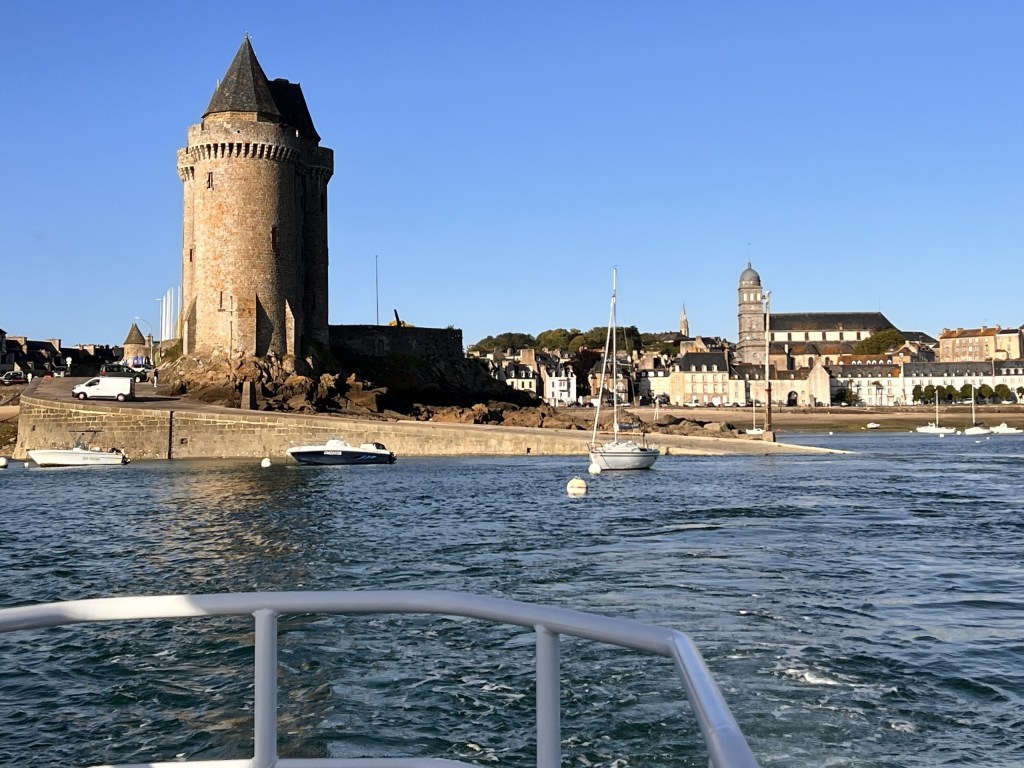 View of a coastal town with a castle tower, boats, and clear blue sky.