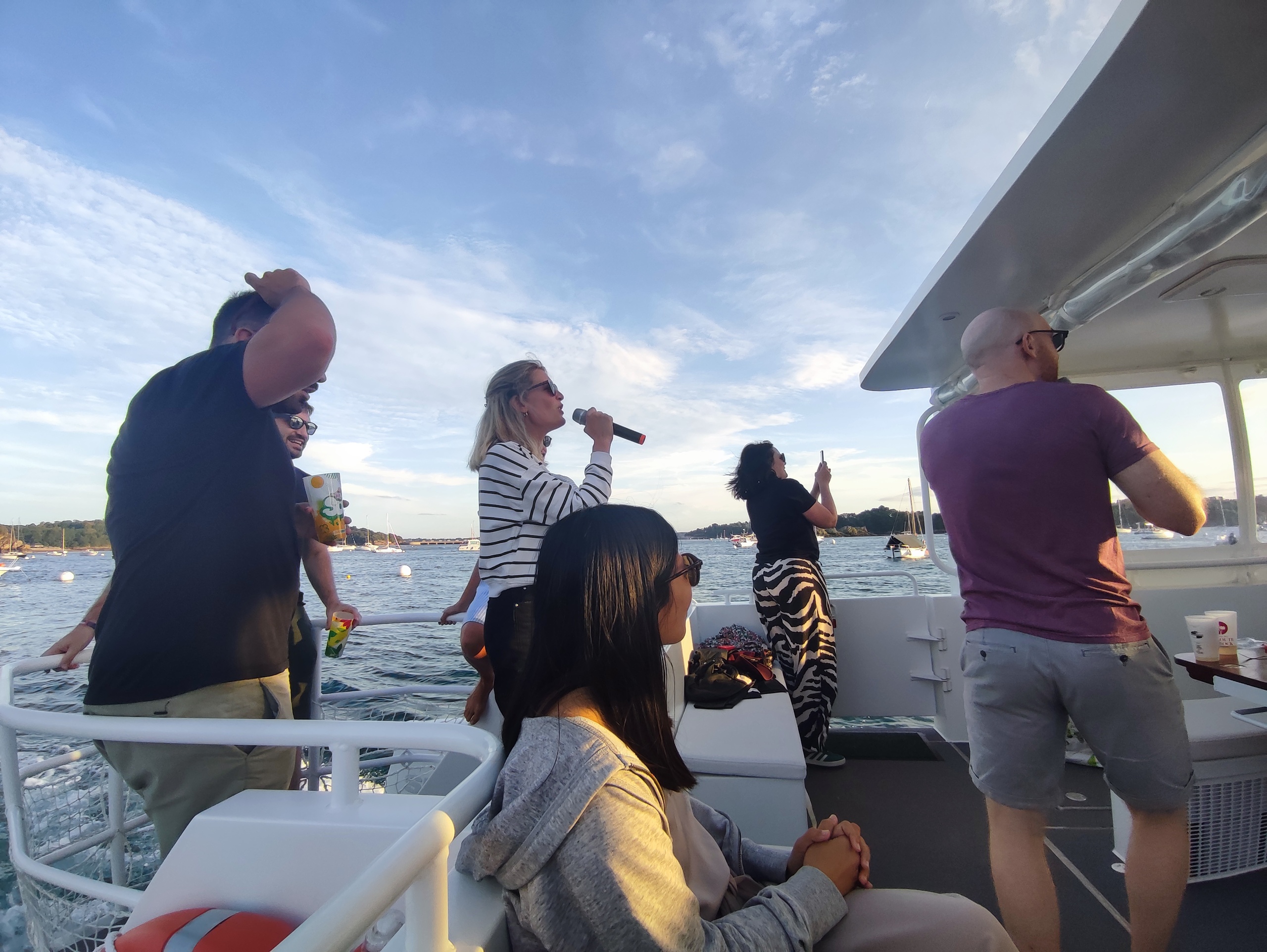 People enjoying a boat party; one woman singing with a microphone.
