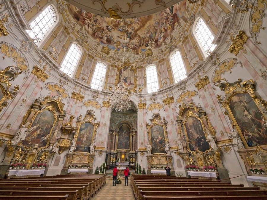 Ornate baroque church interior with paintings, chandeliers, and high ceilings.