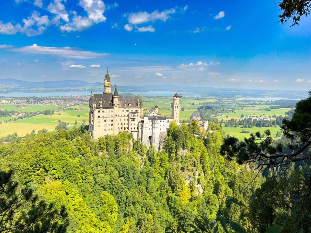 A castle atop a lush, green hill under a blue sky with scattered clouds.