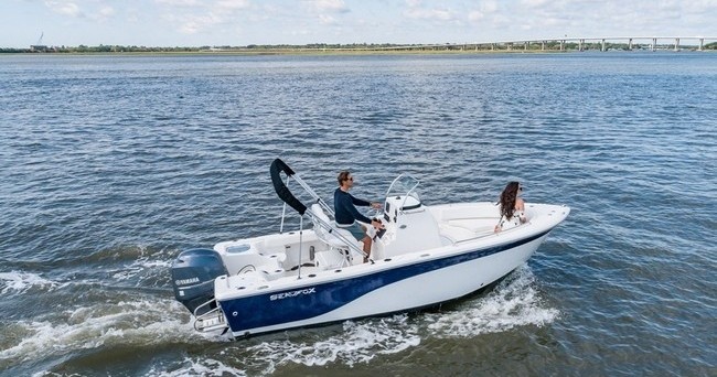 Small motorboat with two people on open water near a riverbank.