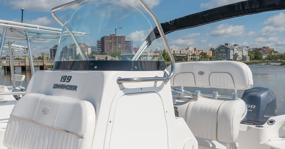 Boat cockpit with white seats and controls, cityscape in background.