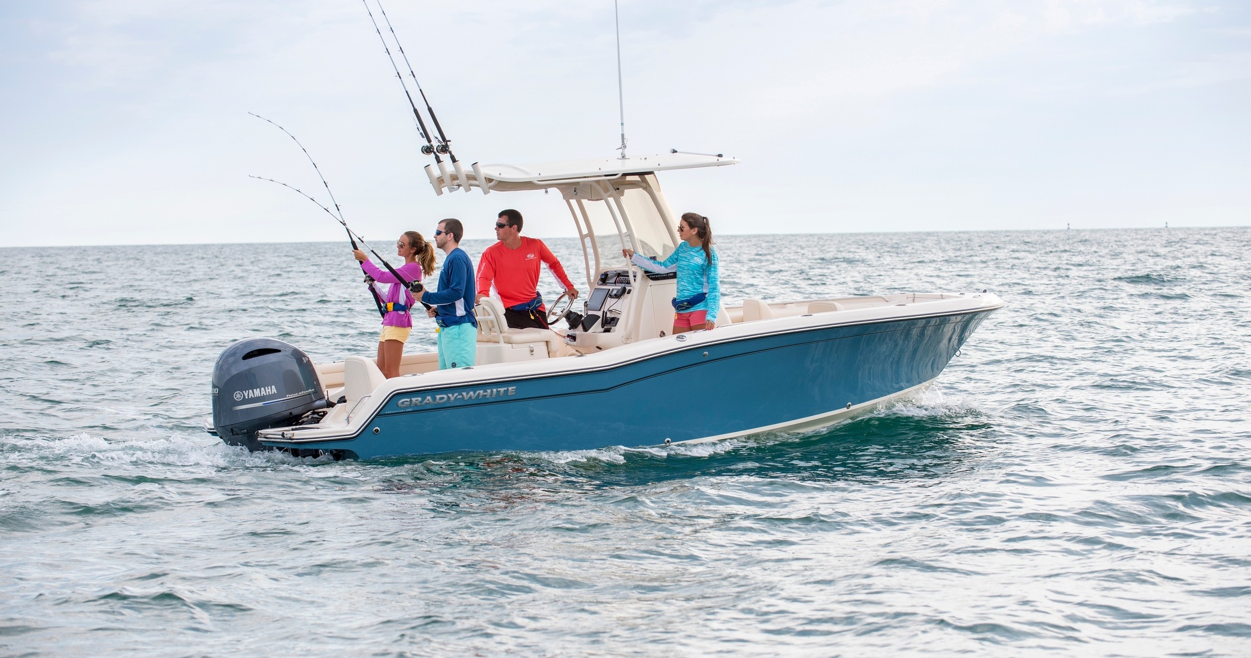 Four people fishing on a blue motorboat in the ocean.
