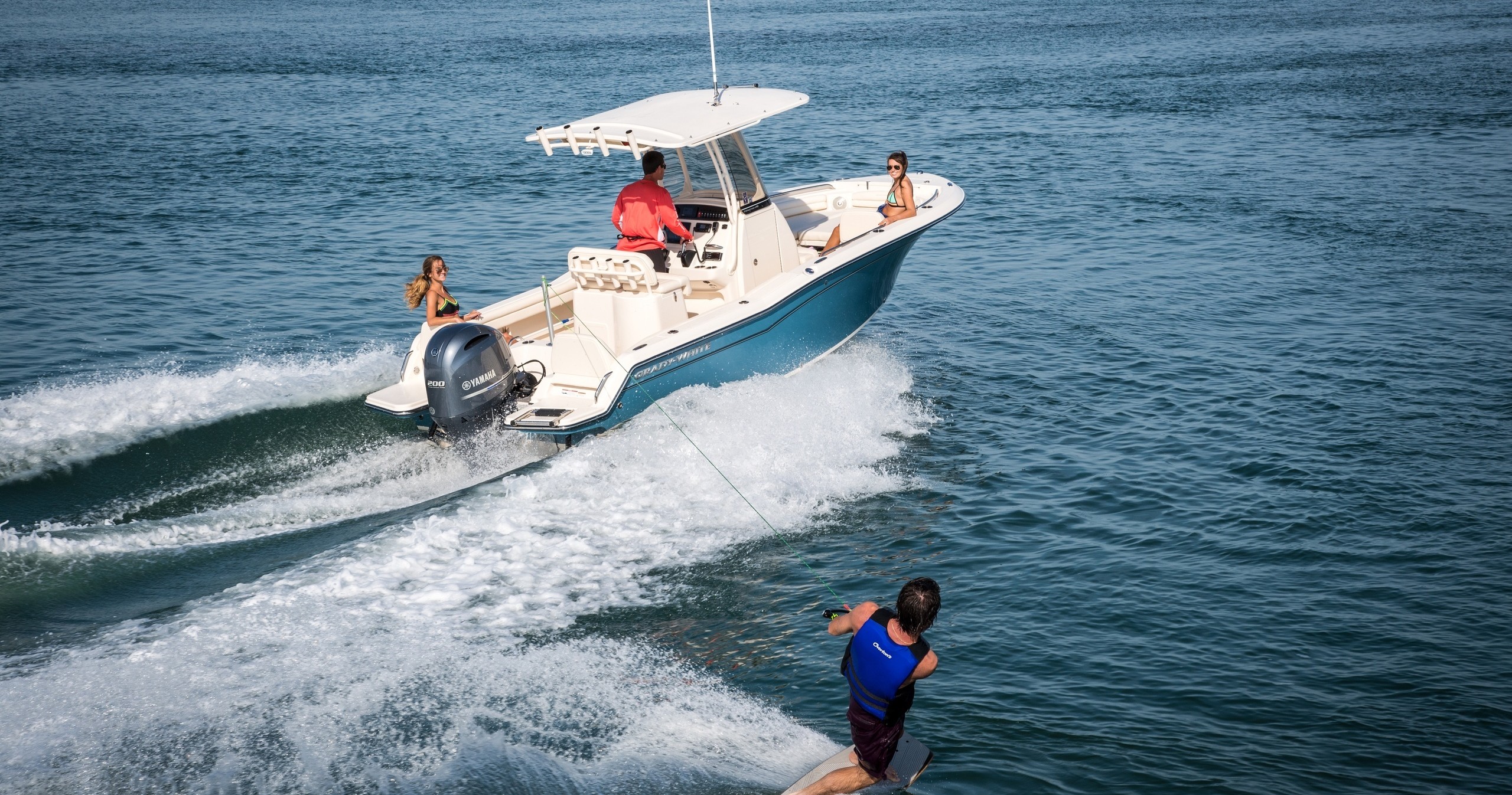 Person wakeboarding behind a motorboat with three people in open water.