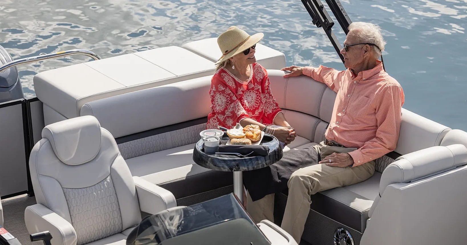 Elderly couple sitting on a boat, talking and enjoying snacks in the sun.