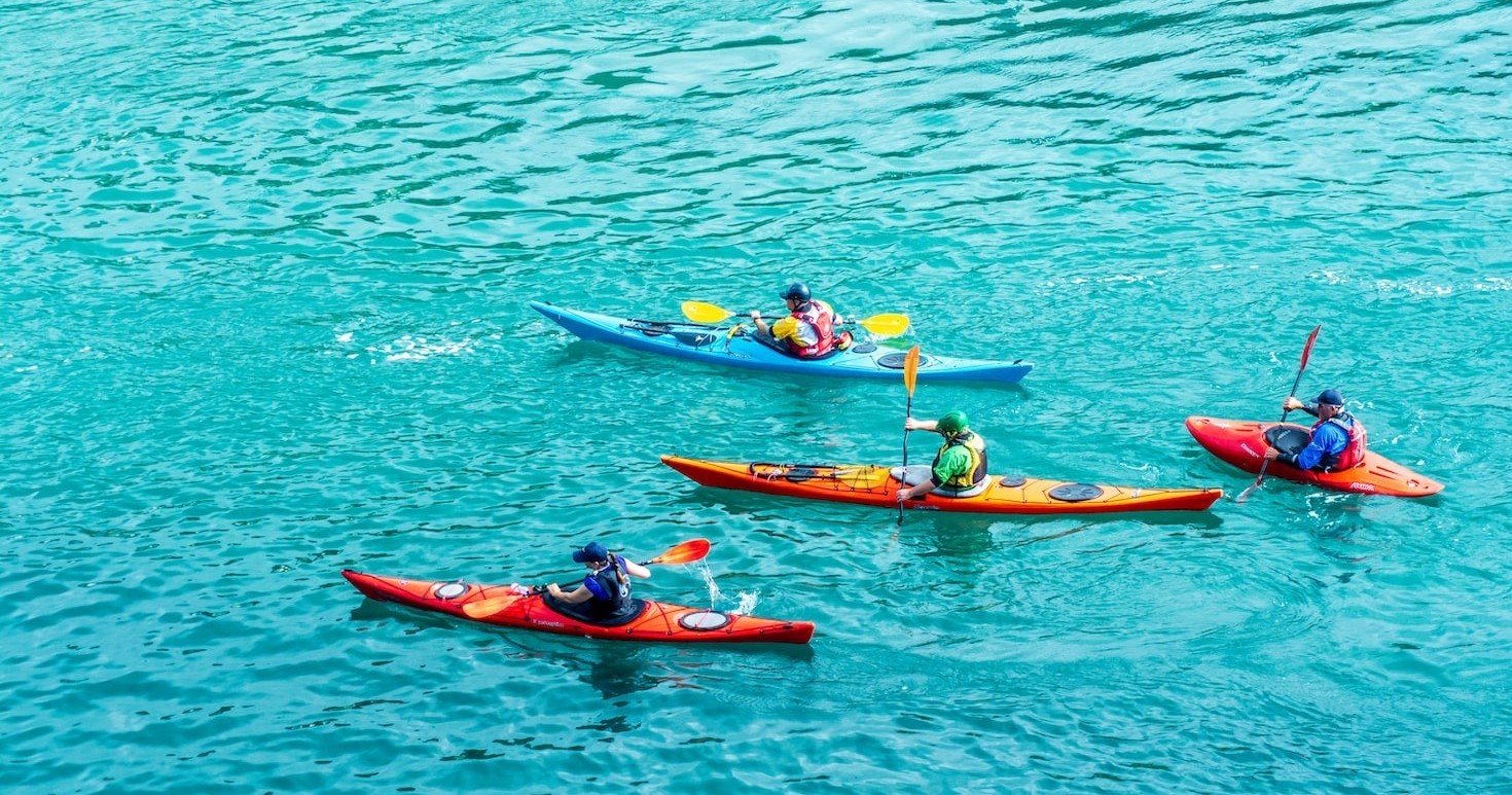 Four people kayaking on clear blue water.