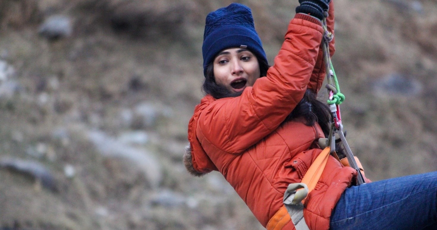 Person ziplining in winter clothing, orange jacket and blue beanie.