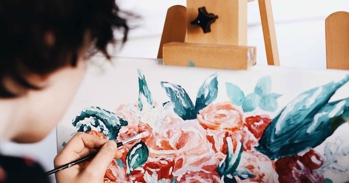 Person painting a floral design on canvas with pink roses and green leaves.