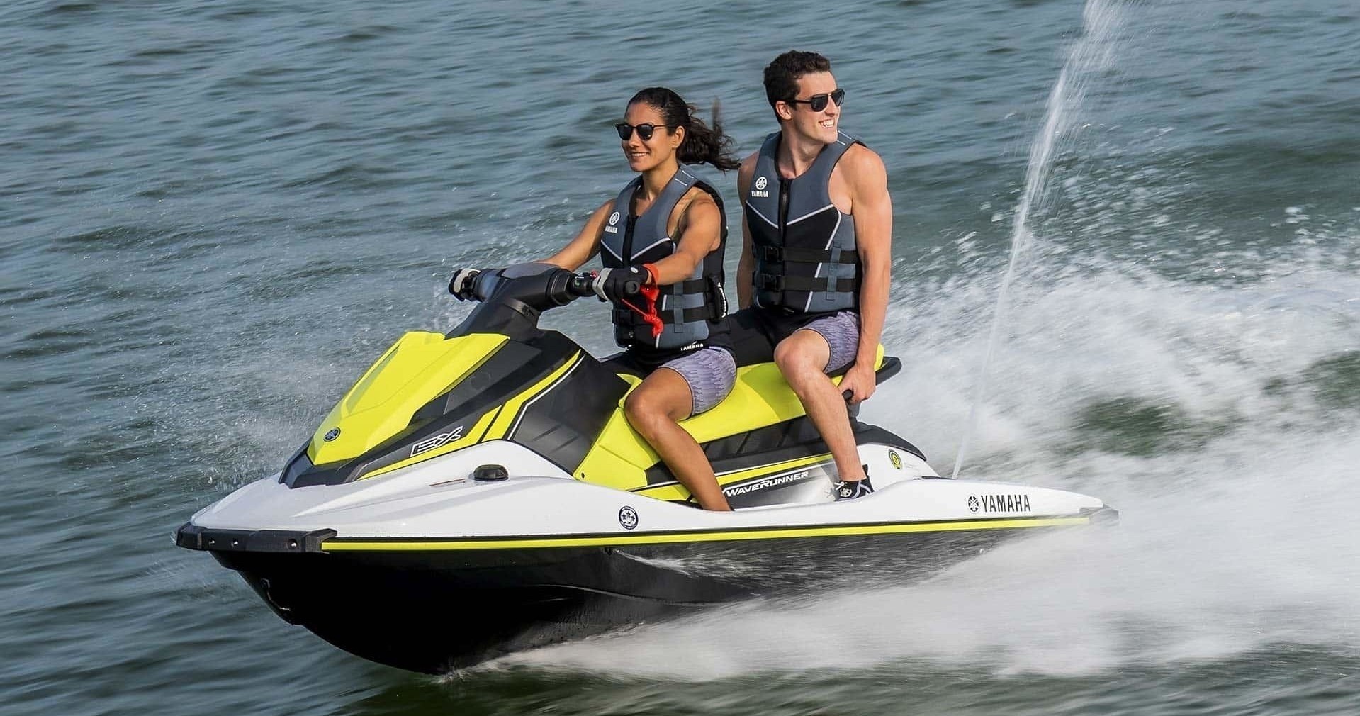 Two people riding a yellow and white jet ski on the water.