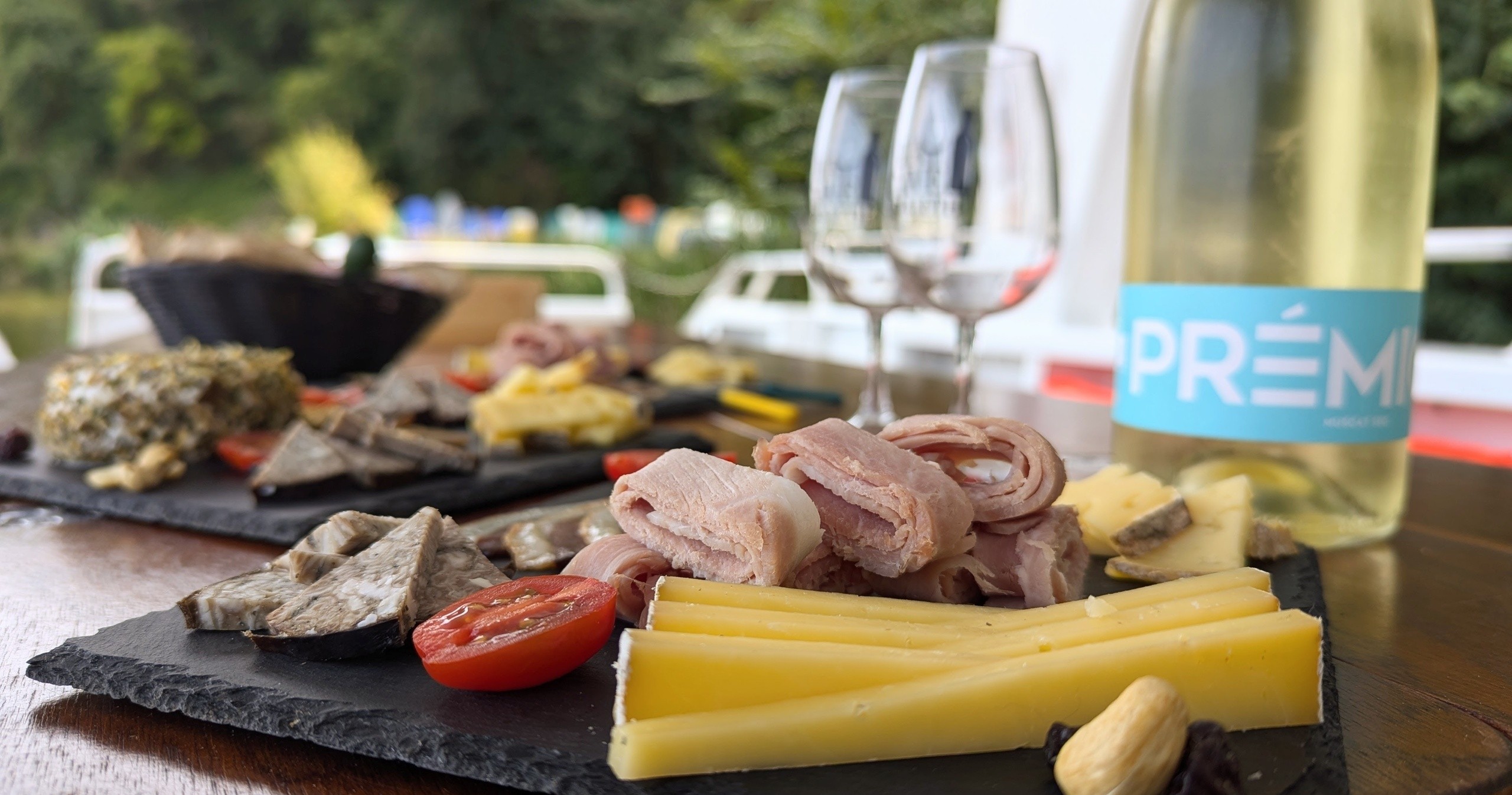 Charcuterie board with meats, cheese, tomatoes, wine glasses, and bottle on a table outdoors.