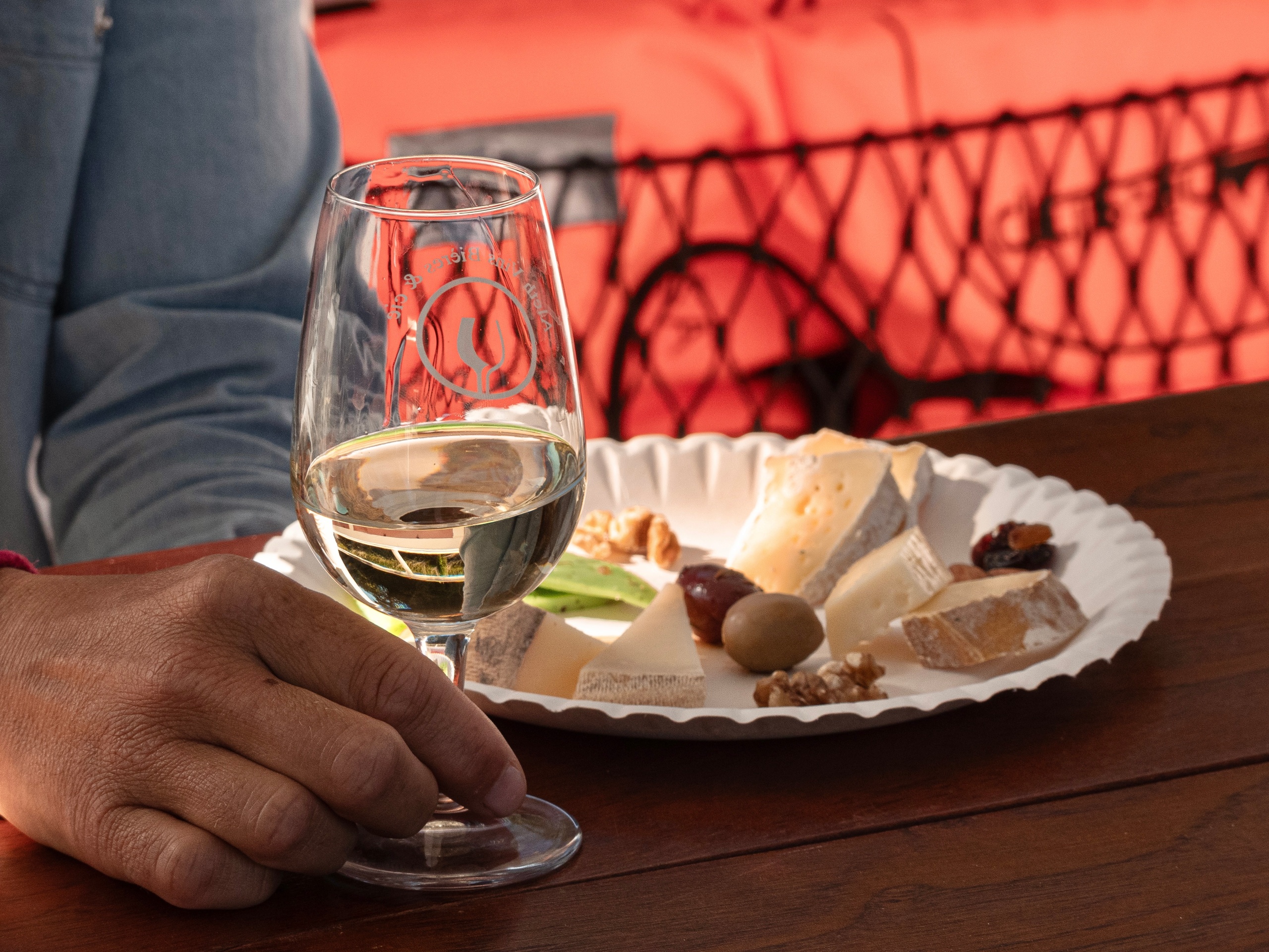 Person holding wine glass beside plate of cheese and snacks.