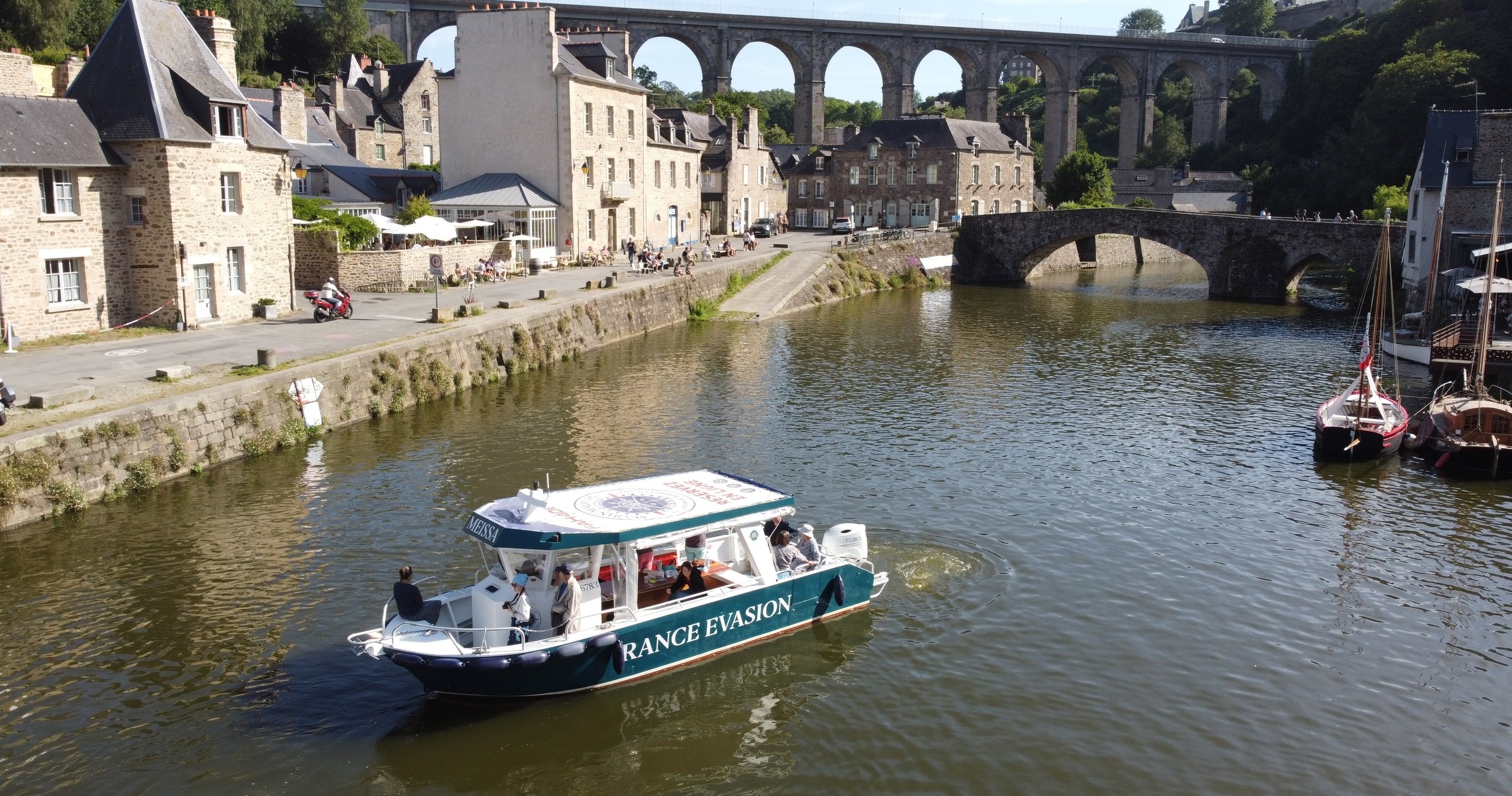 Tour boat on river near stone buildings and arched bridge.