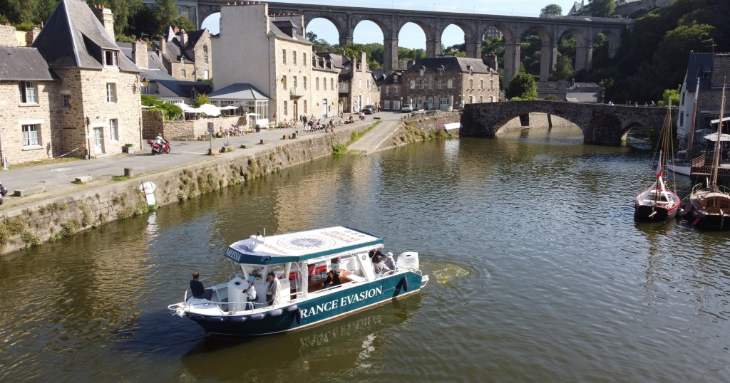 Tour boat on river near stone buildings and arched bridge.