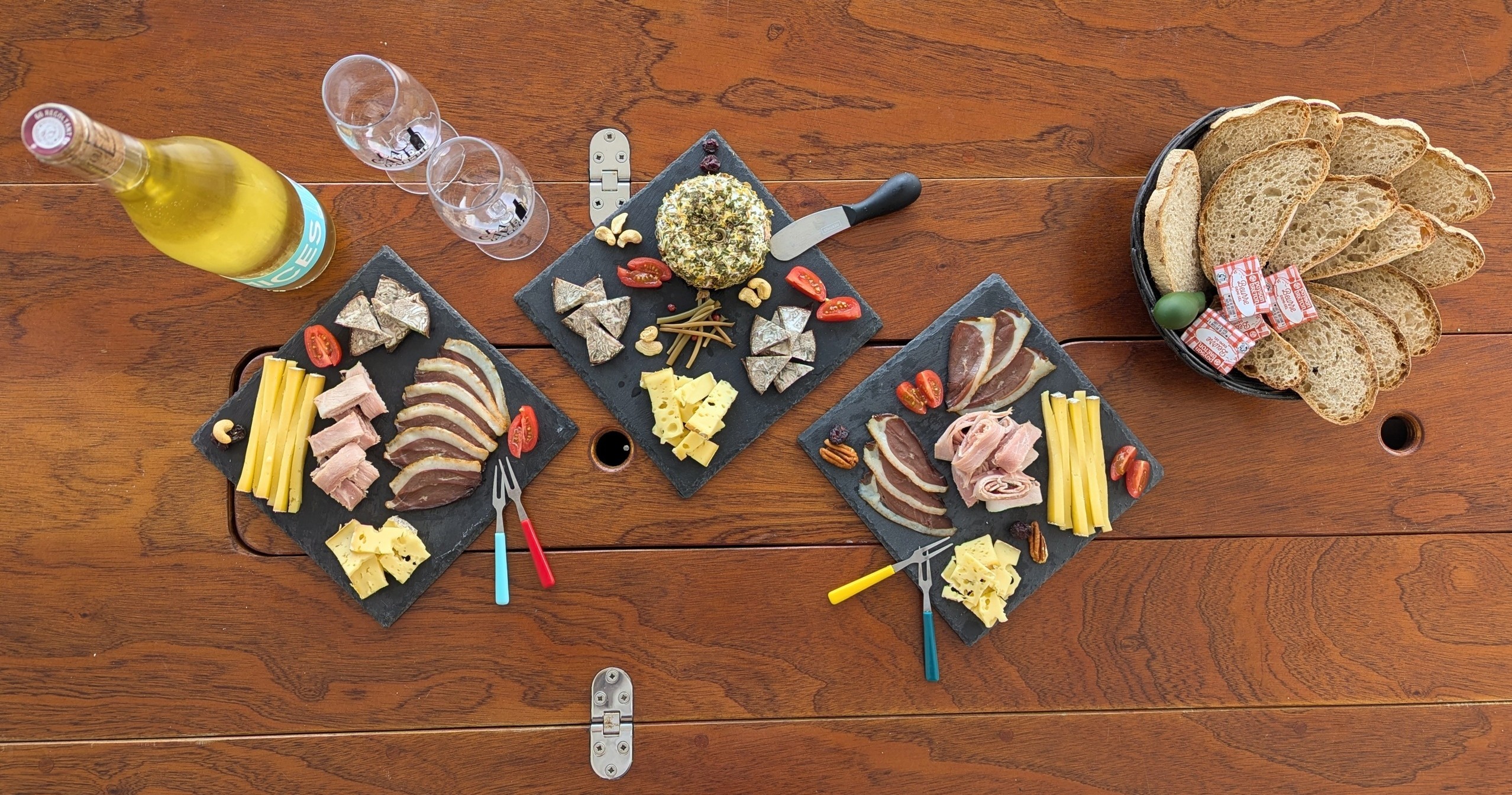 Charcuterie spread on wooden table with wine, bread, and cheese.