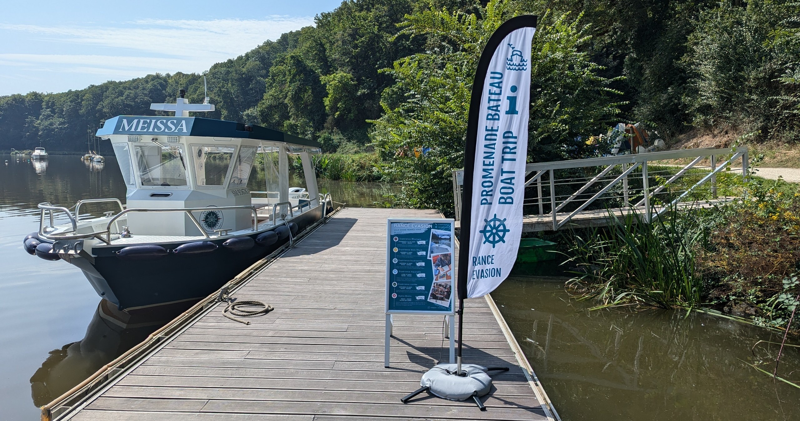 Boat named 'MEISSA' docked at a pier beside a sign and greenery.