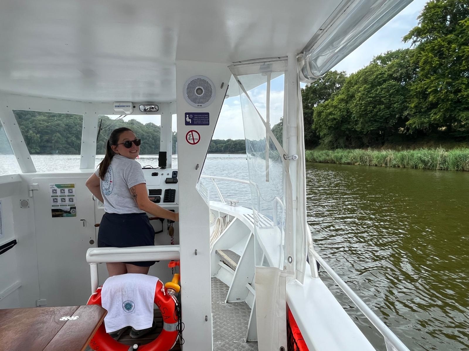 Person steering a boat on a river with trees on the bank.