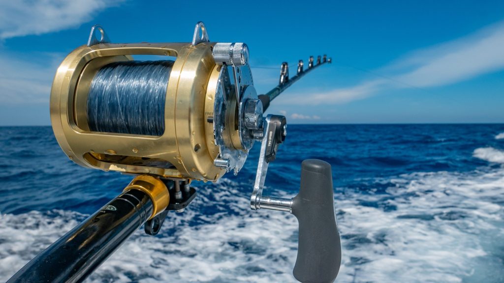 Fishing rod with reel over ocean waves under a clear blue sky.