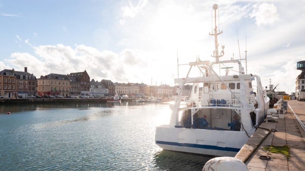 Fishing boat docked at a sunny harbor with buildings in the background.
