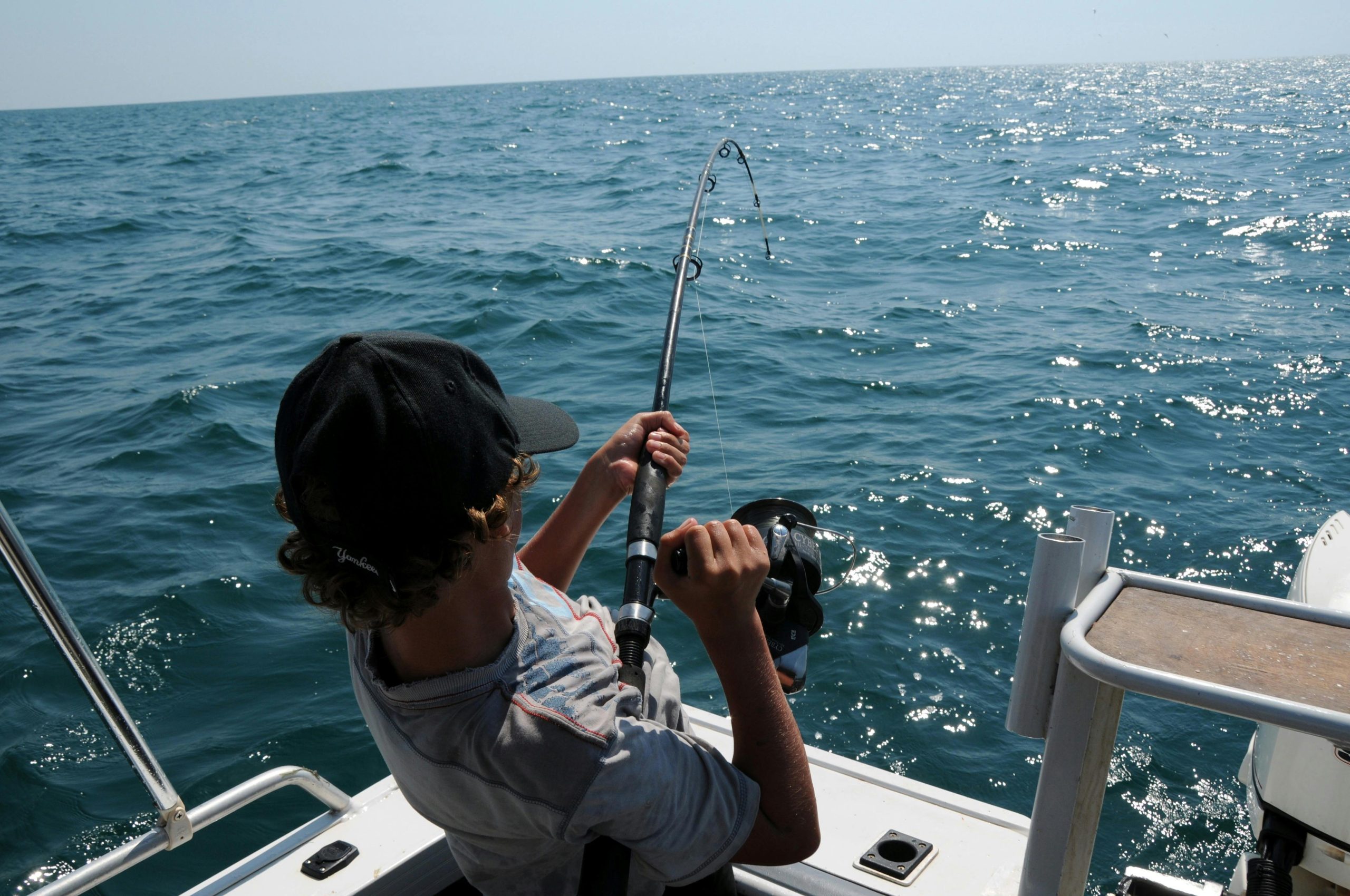 Person fishing from a boat on a sunny ocean day.