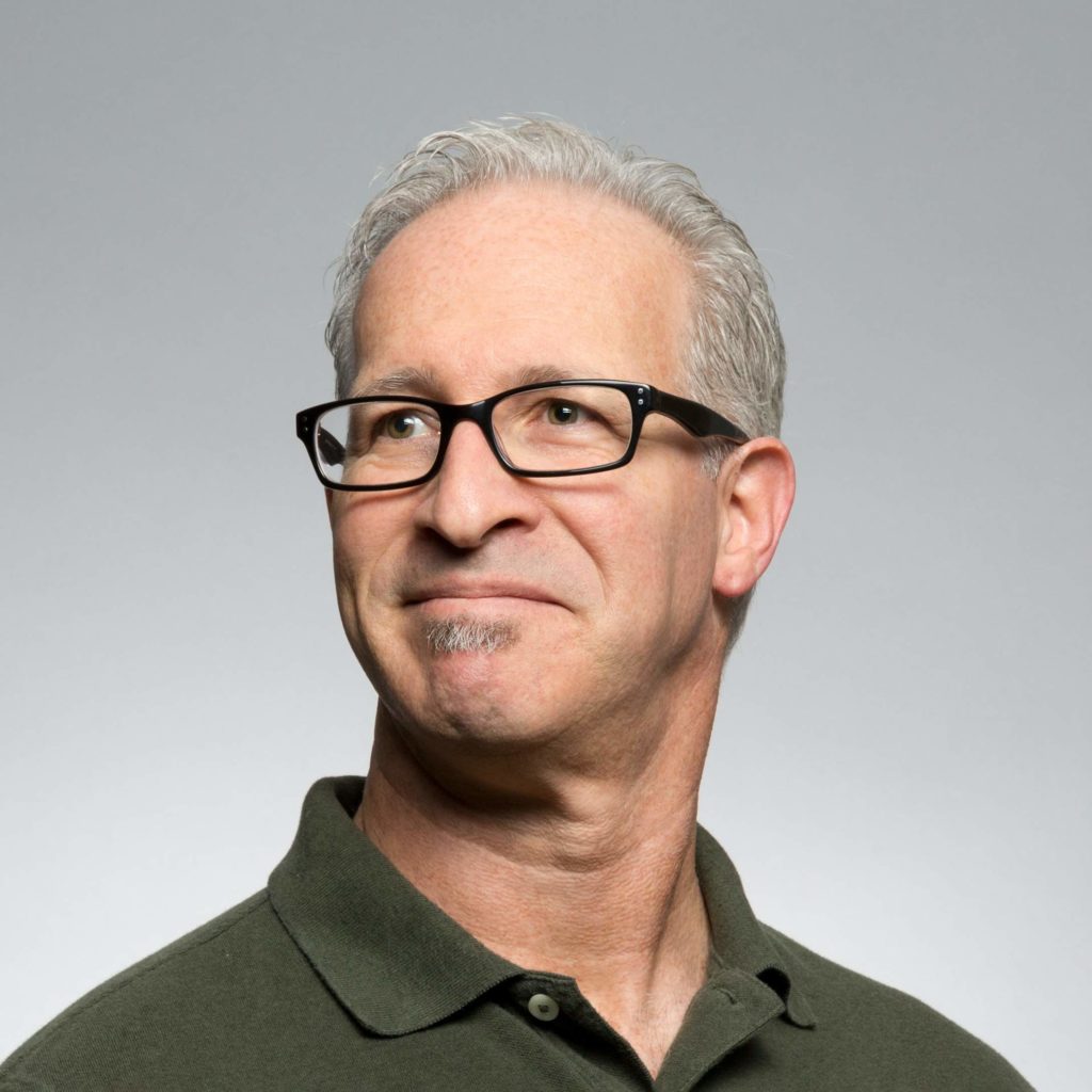 Smiling man with glasses looking to the side against gray background.