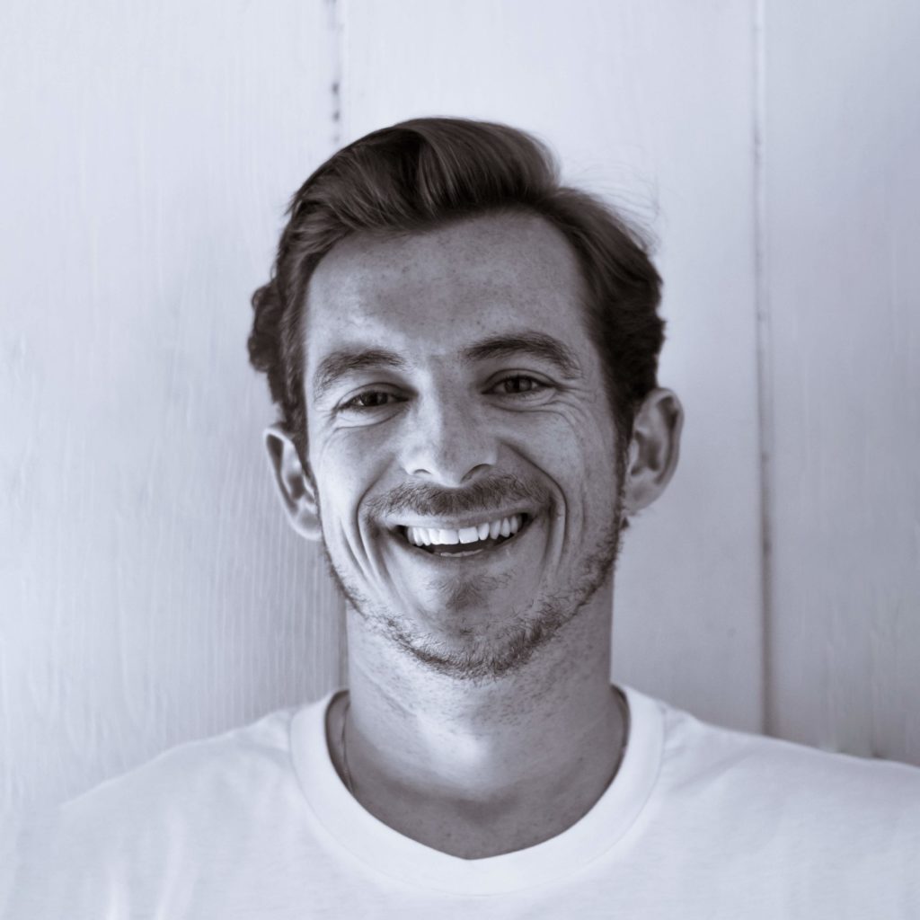 Smiling man with short hair in a white shirt against wood background.