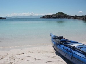 Blue kayak on a sandy beach with calm sea and distant hills.