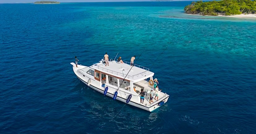 People on a boat near a tropical island in blue ocean waters.