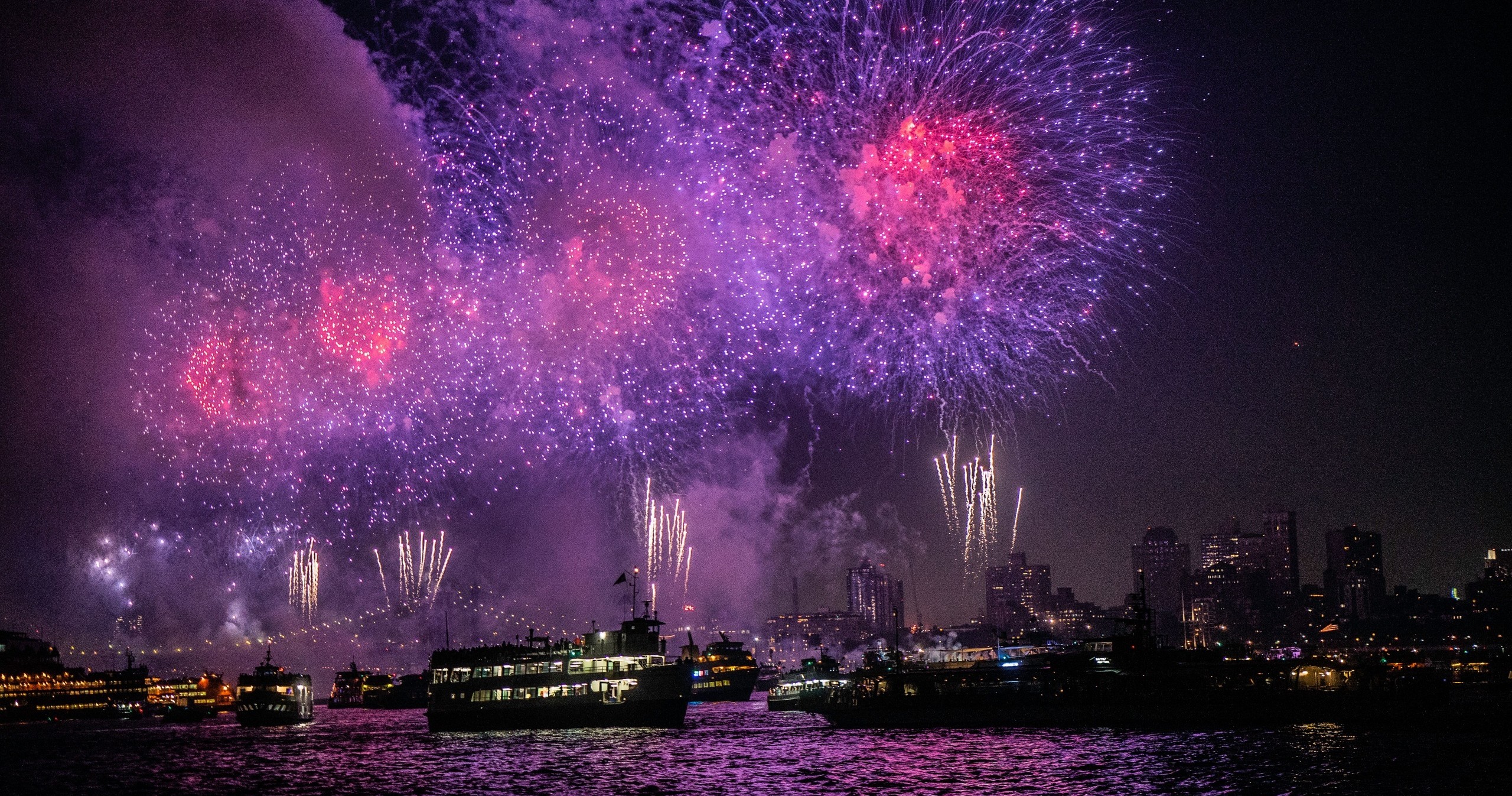 Colorful fireworks over a city skyline and river at night.