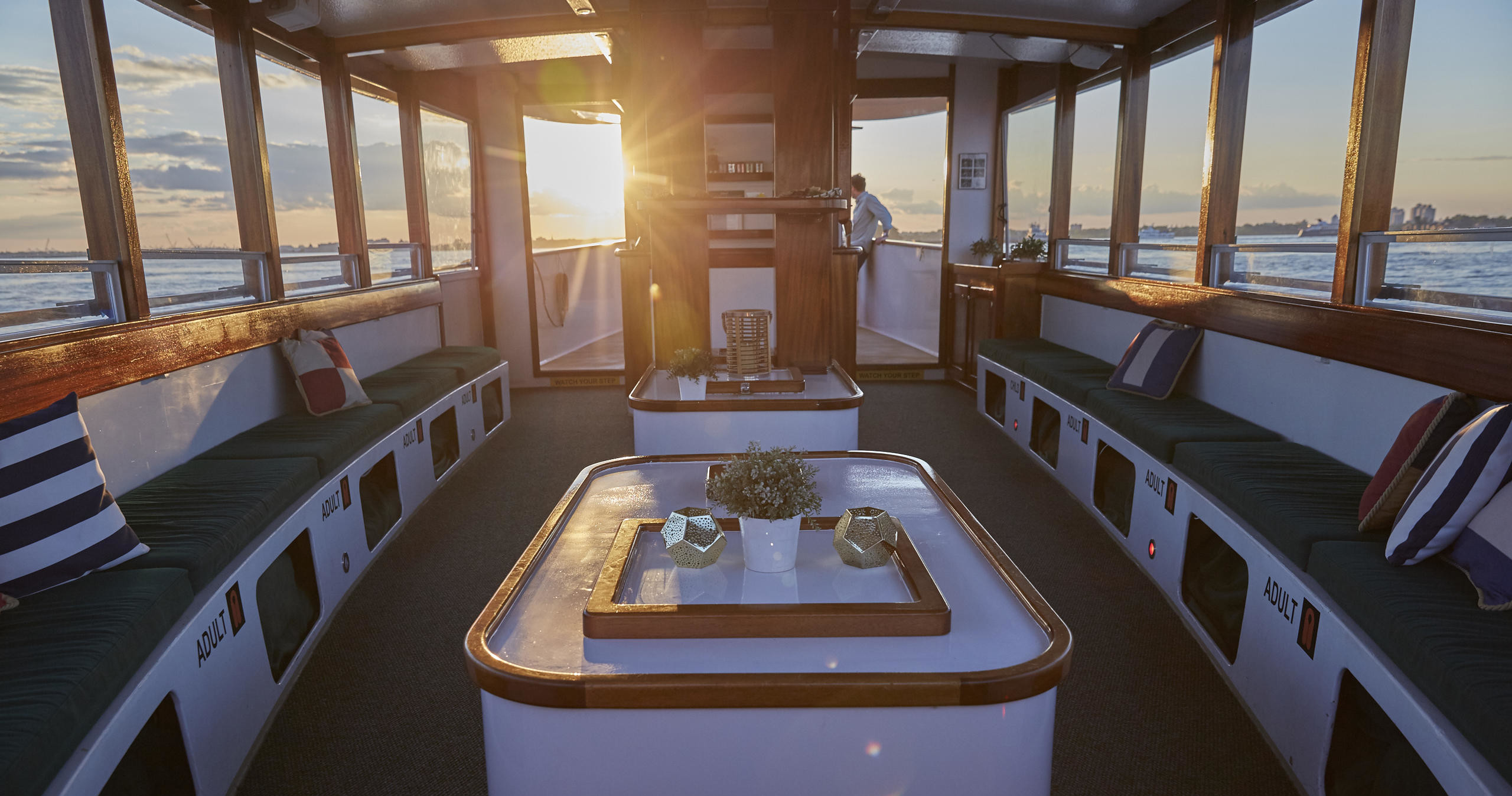 Interior of a boat cabin at sunset with benches and cushions.