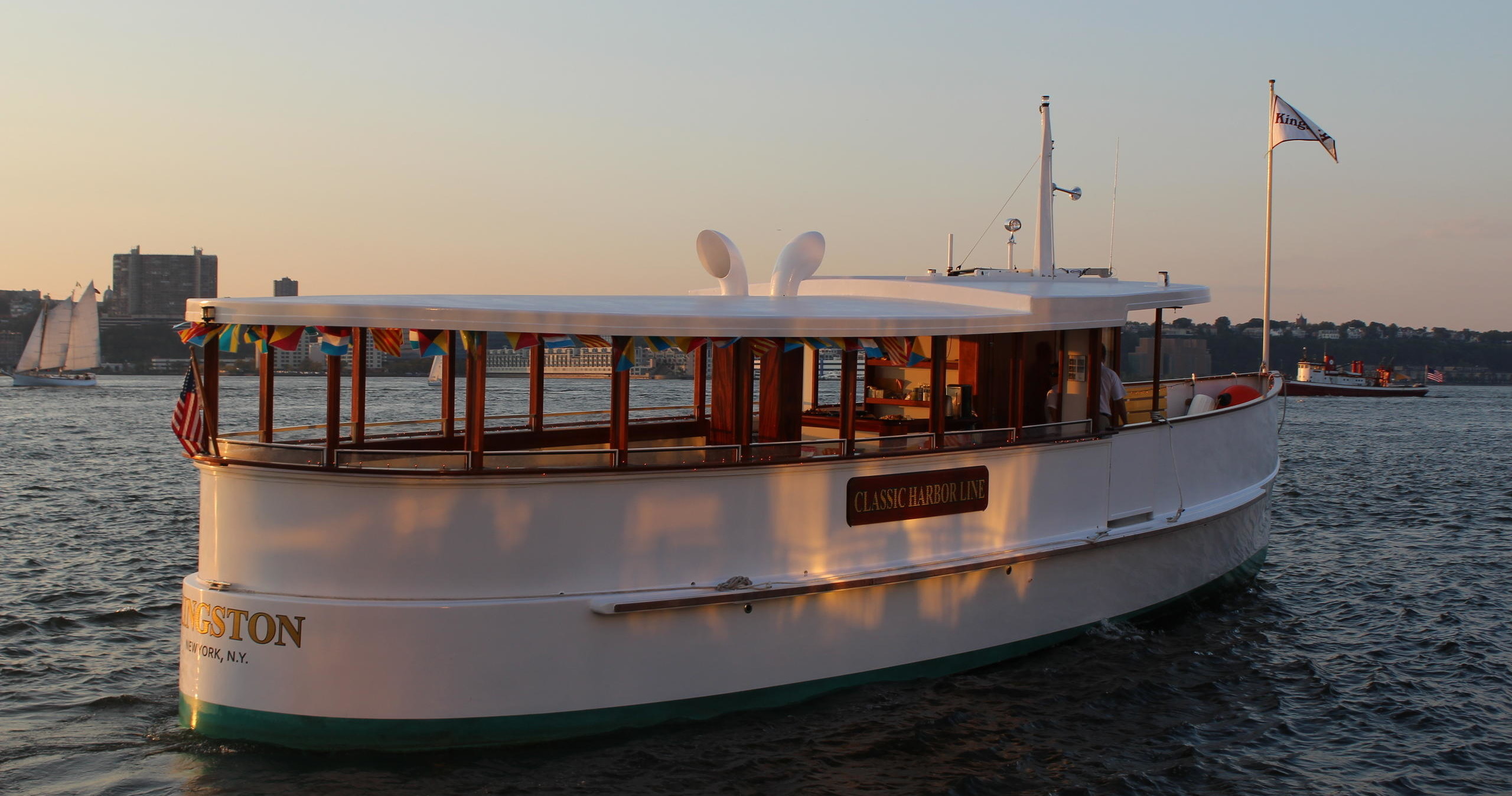 White boat on water during sunset with city skyline in background.
