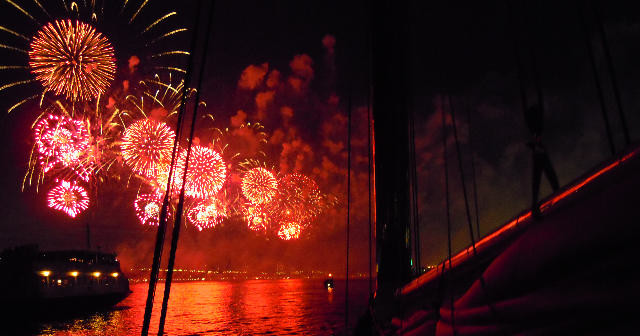 Bright fireworks over water at night with ship silhouettes.