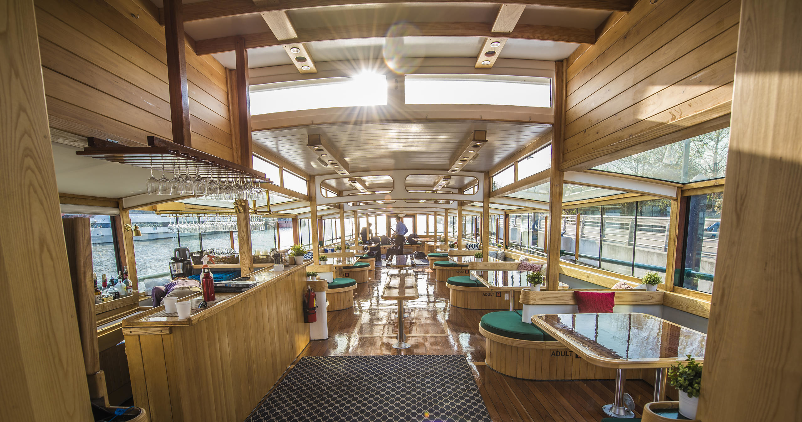 Interior of a sunlit, wood-paneled boat with tables and windows.