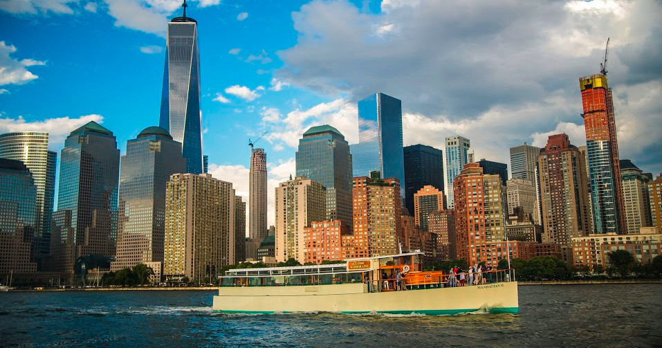 Ferry on water with New York City skyline and One World Trade Center in the background.