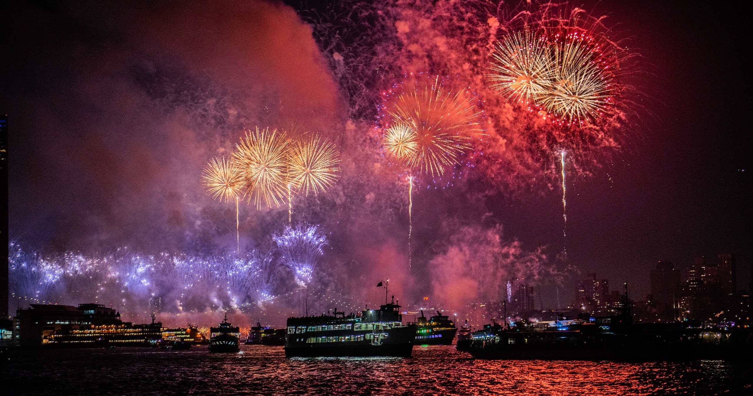 Colorful fireworks over a city waterfront at night with boats.