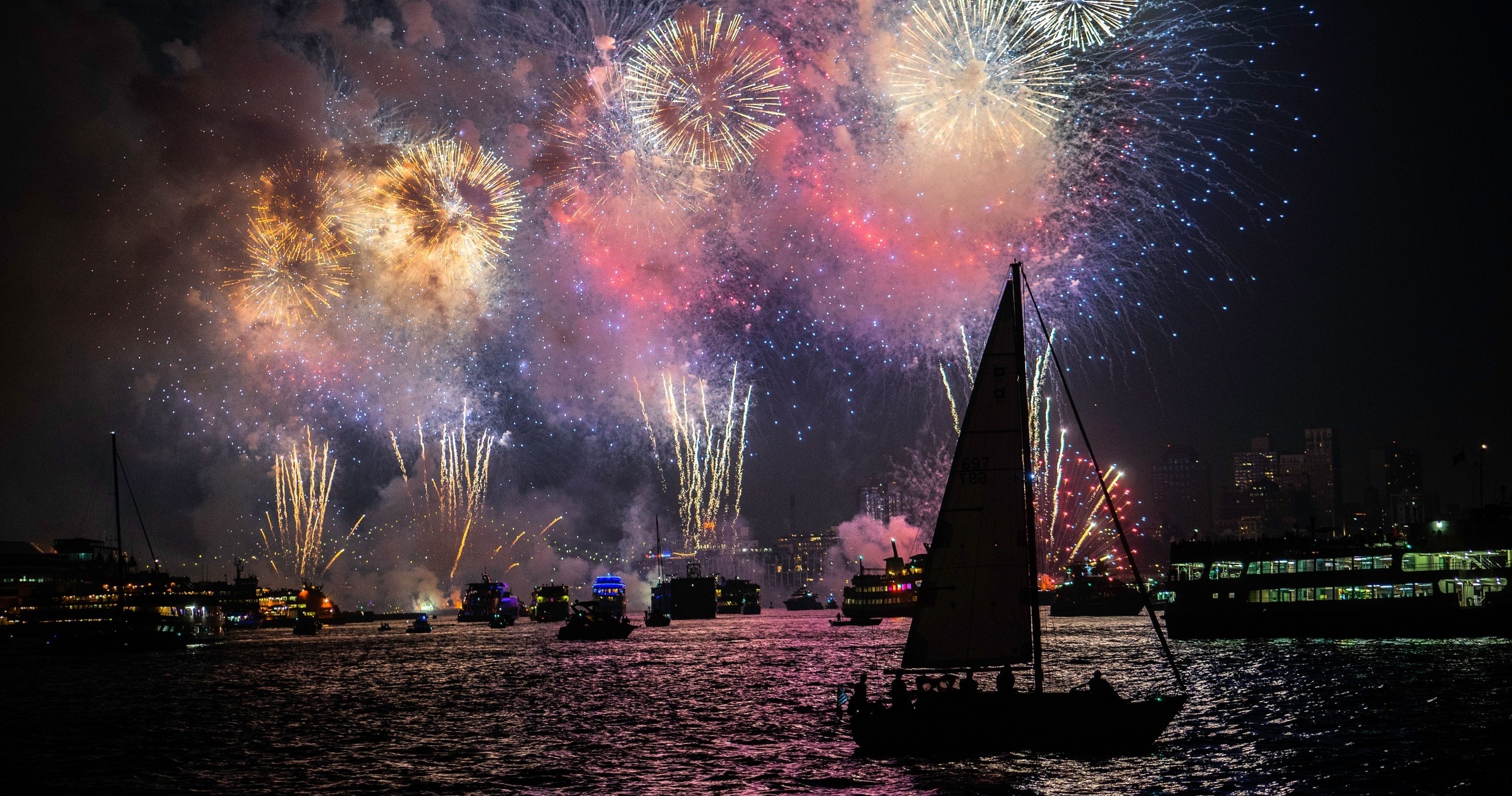 Colorful fireworks over a harbor with boats on the water at night.