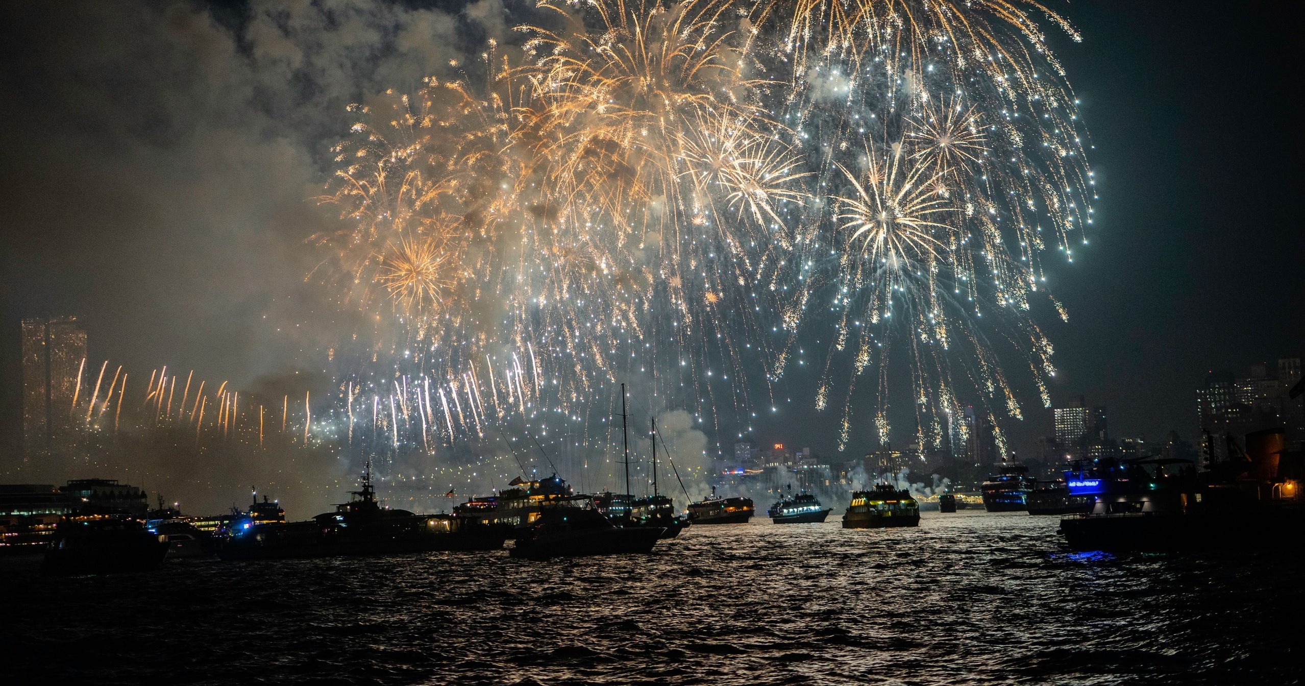 Fireworks over a harbor with boats at night.