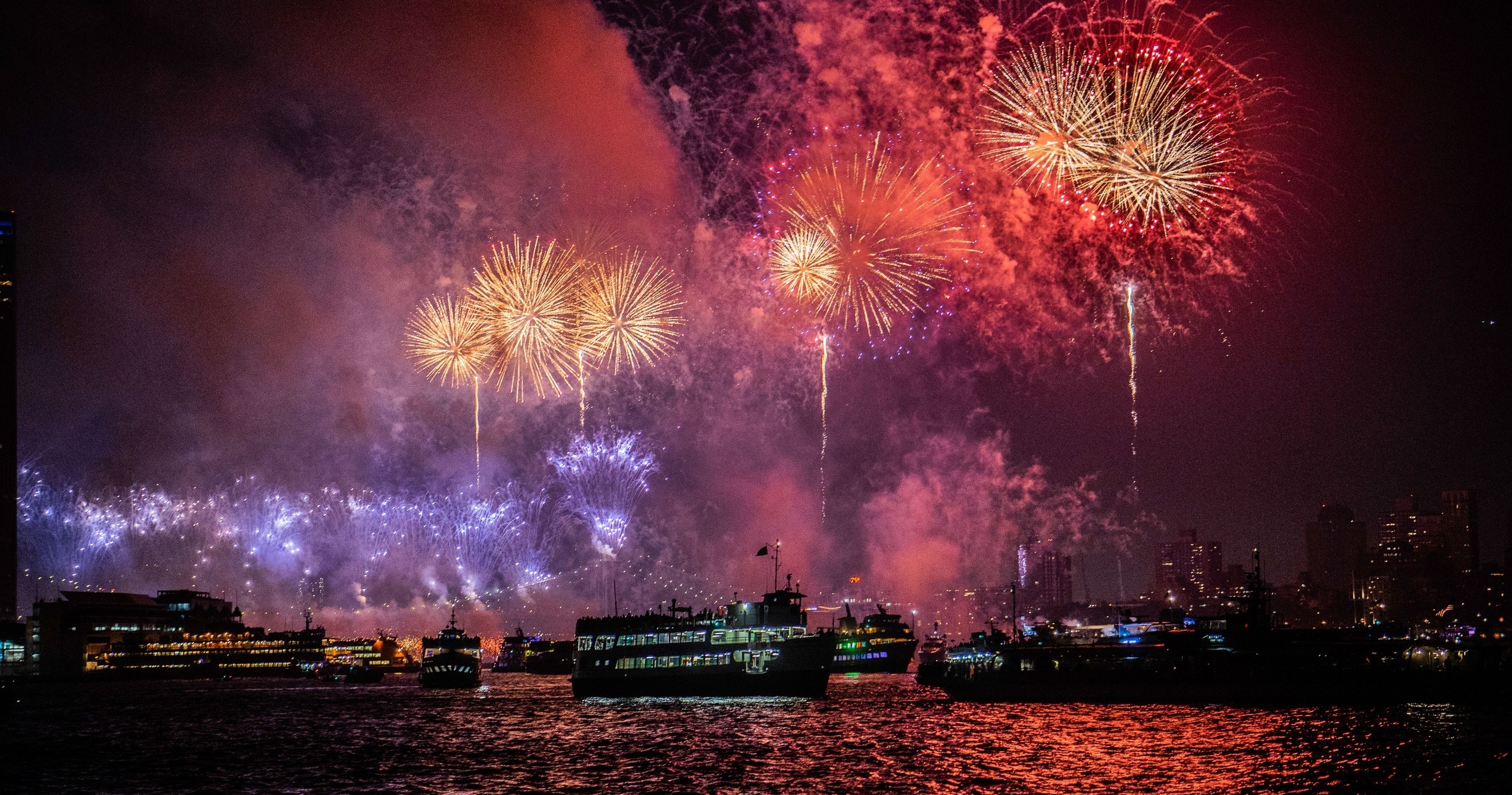 Boats on water under colorful fireworks in the night sky.