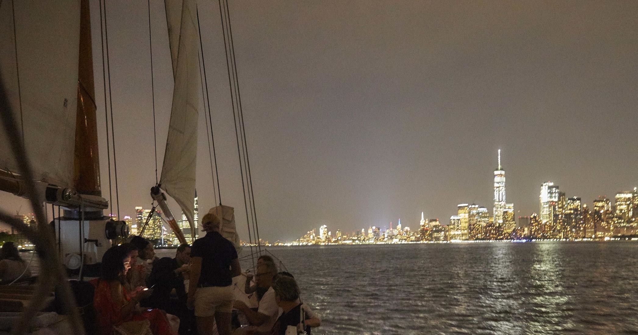 People on a boat at night with city skyline in the background.