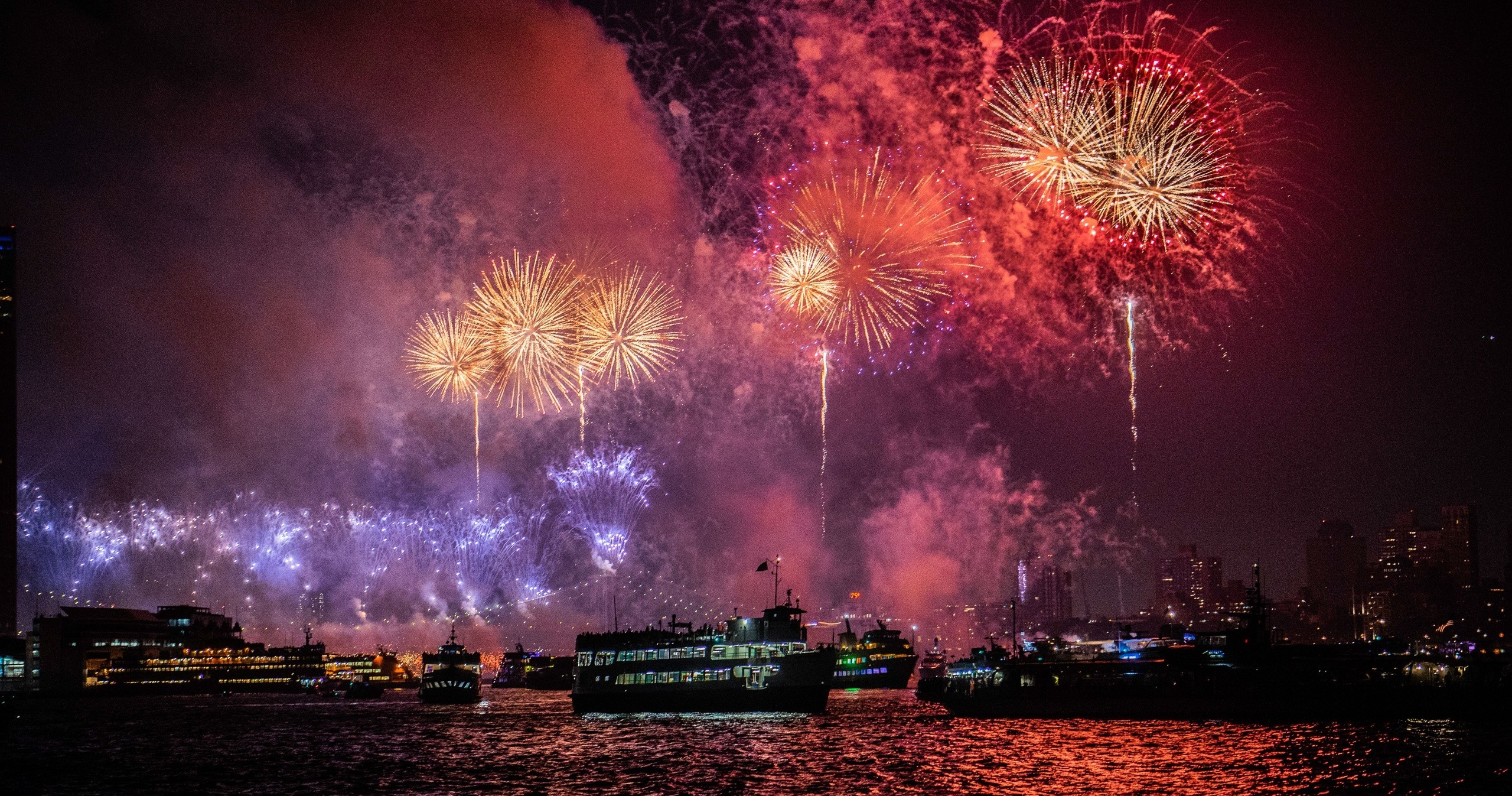 Colorful fireworks over a city harbor with silhouetted boats.