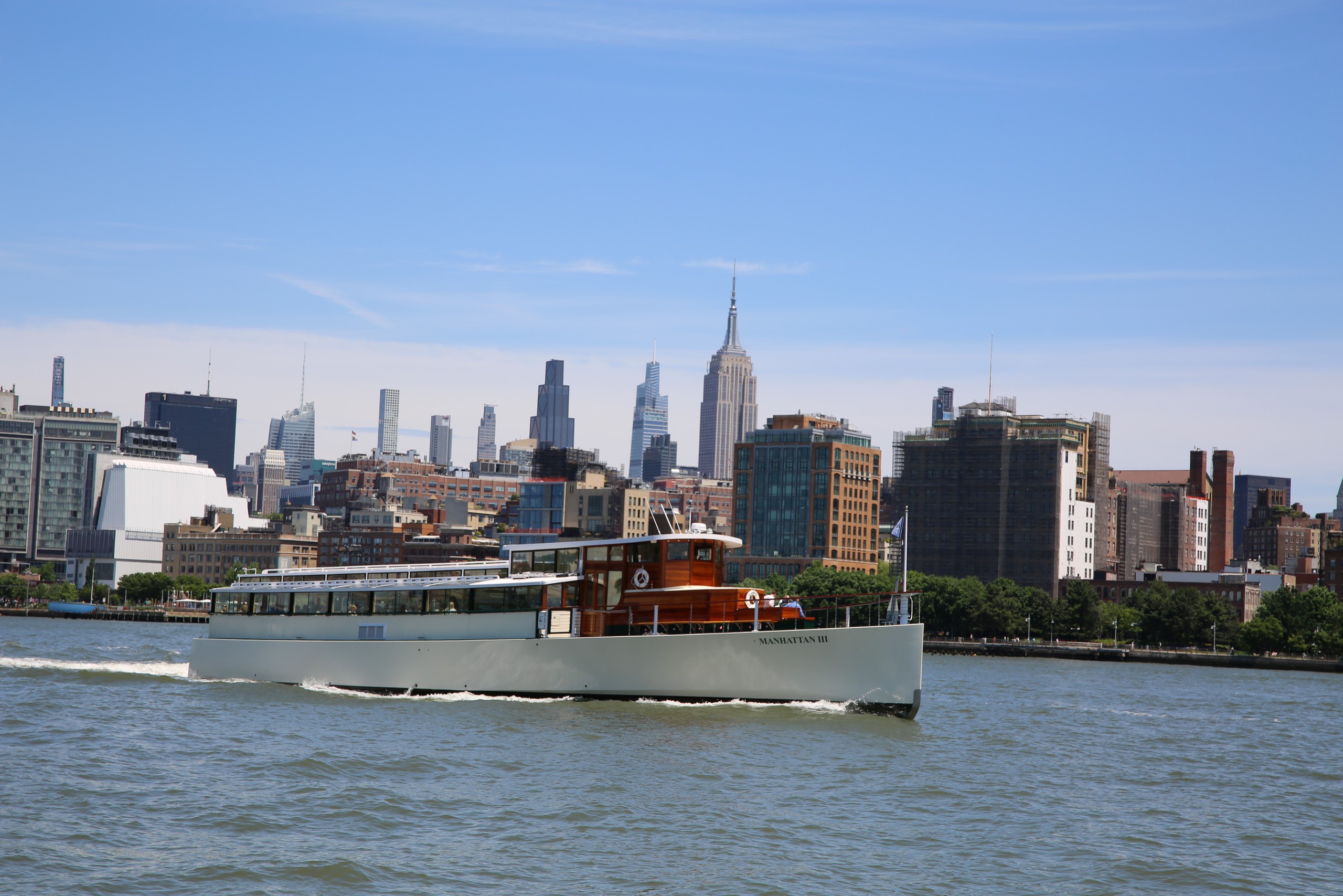 Boat sailing on a river with city skyline, including tall buildings, in the background.